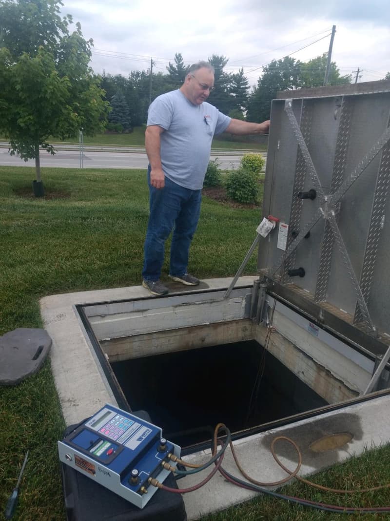 Plumber beside open backflow vault with test kit